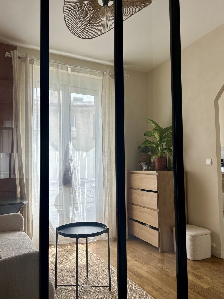 Studio parisien 21m² – verrière noire séparant le salon cosy et la chambre avec lit bois clair
