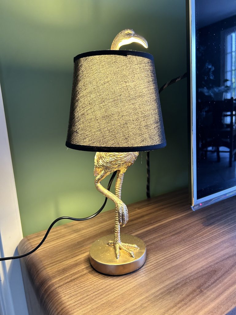 Lampe dorée en forme de flamant avec abat-jour noir sur meuble en noyer détail décoratif d’un salon Art Déco