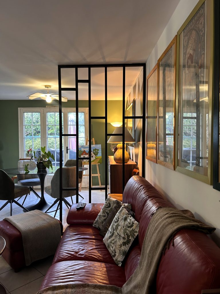Salle à manger avec table ovale en verre texturé et plante décorative, donnant sur de grandes portes-fenêtres